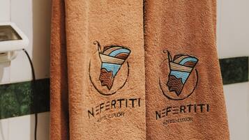 Two brown towels hanging on a white towel rack with a green stripe, featuring embroidered logos and text.