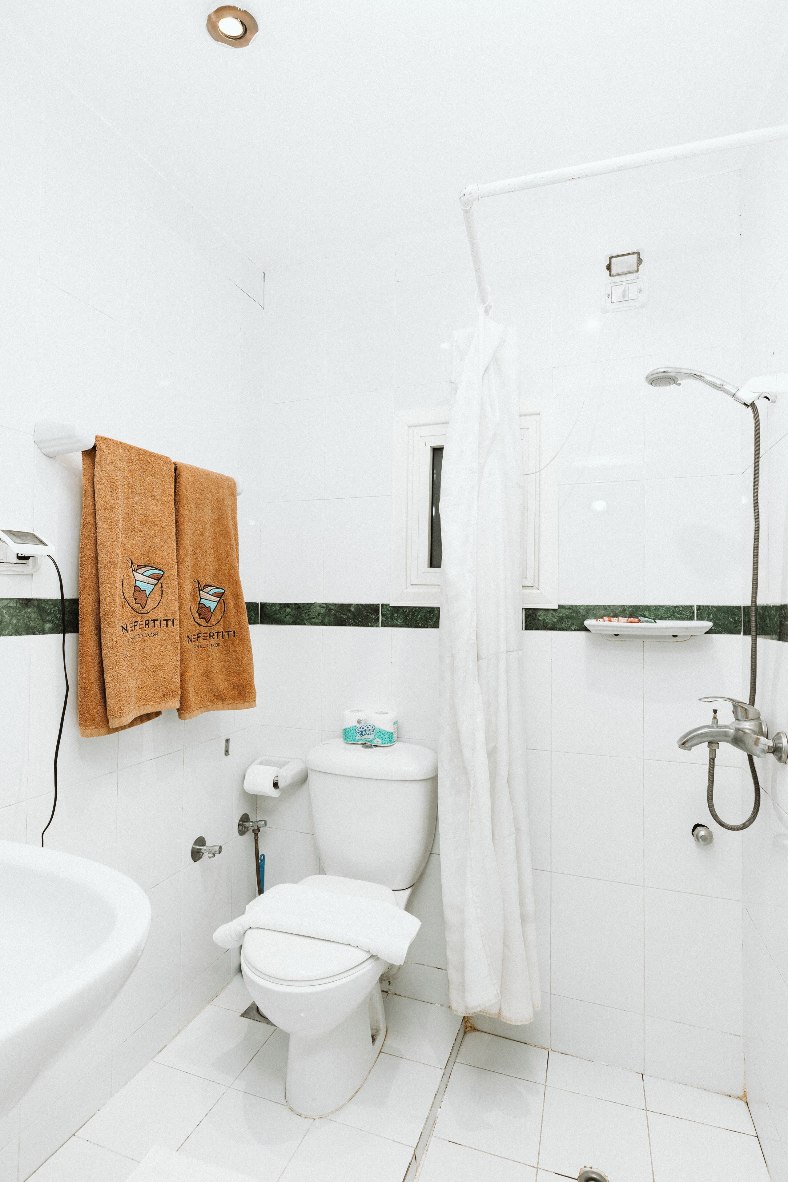 A bathroom with a toilet, sink, and shower. There are towels hanging on the wall.
