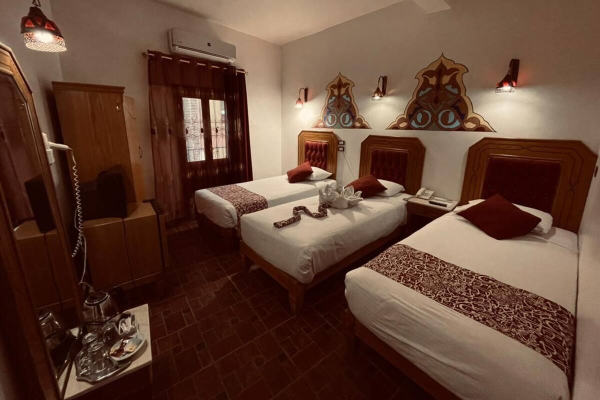 A hotel room with three beds, a desk with a telephone, and decorative wall art.
