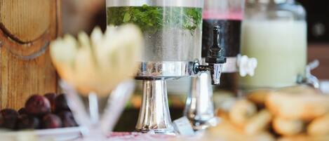 Un dispensador de bebidas con un recipiente transparente y un caño de metal, rodeado de diversos alimentos y un fondo de madera.