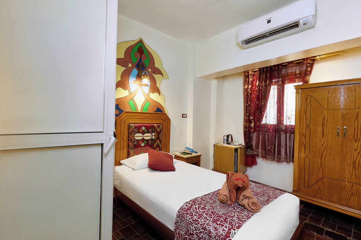 A hotel room with a bed, a wardrobe, a nightstand, and a decorative wall piece.