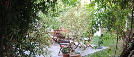 Un espace patio aménagé avec des chaises en bois et des plantes en pot, entouré de verdure.