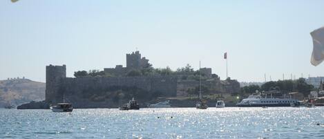 A coastal scene with a castle on a hill, boats on the water, and a clear sky.