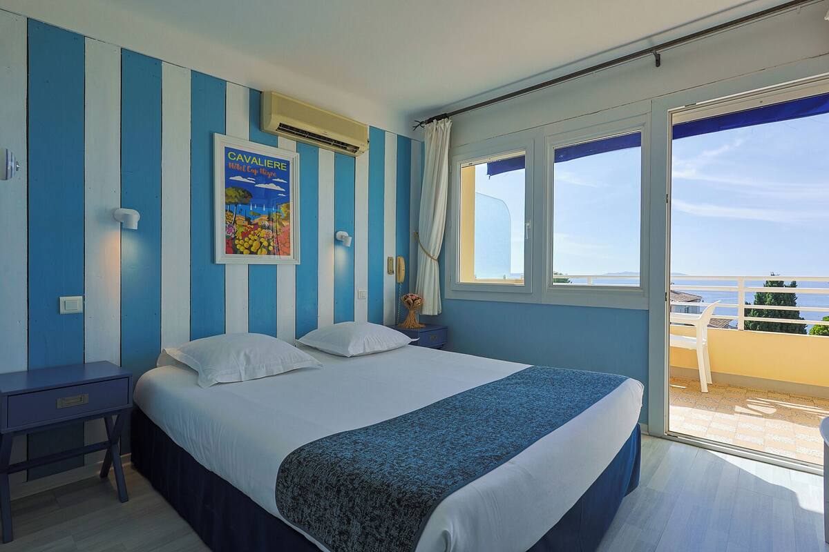 Une chambre à coucher avec un lit, une table de chevet, une affiche et une fenêtre donnant sur la mer.