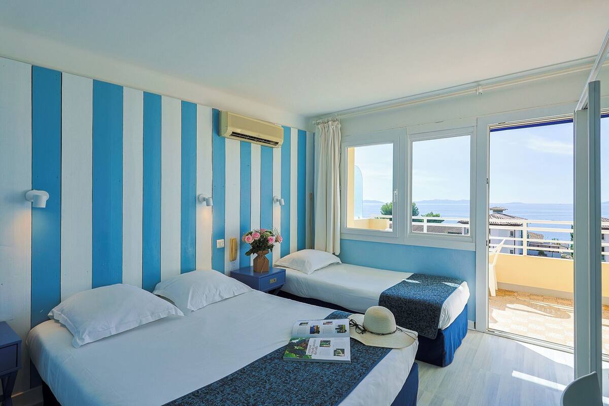 Une chambre d’hôtel avec deux lits, une grande fenêtre donnant sur la mer et un balcon.