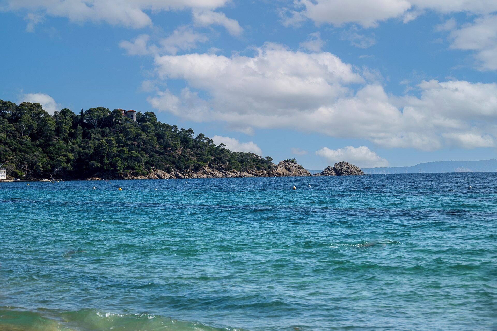 Eine Küstenlandschaft mit klarem, blauem Wasser, Felsformationen und einem bewaldeten Hügel.