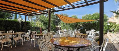 Un patio al aire libre con mesas redondas y sillas blancas, cubierto por una marquesina.