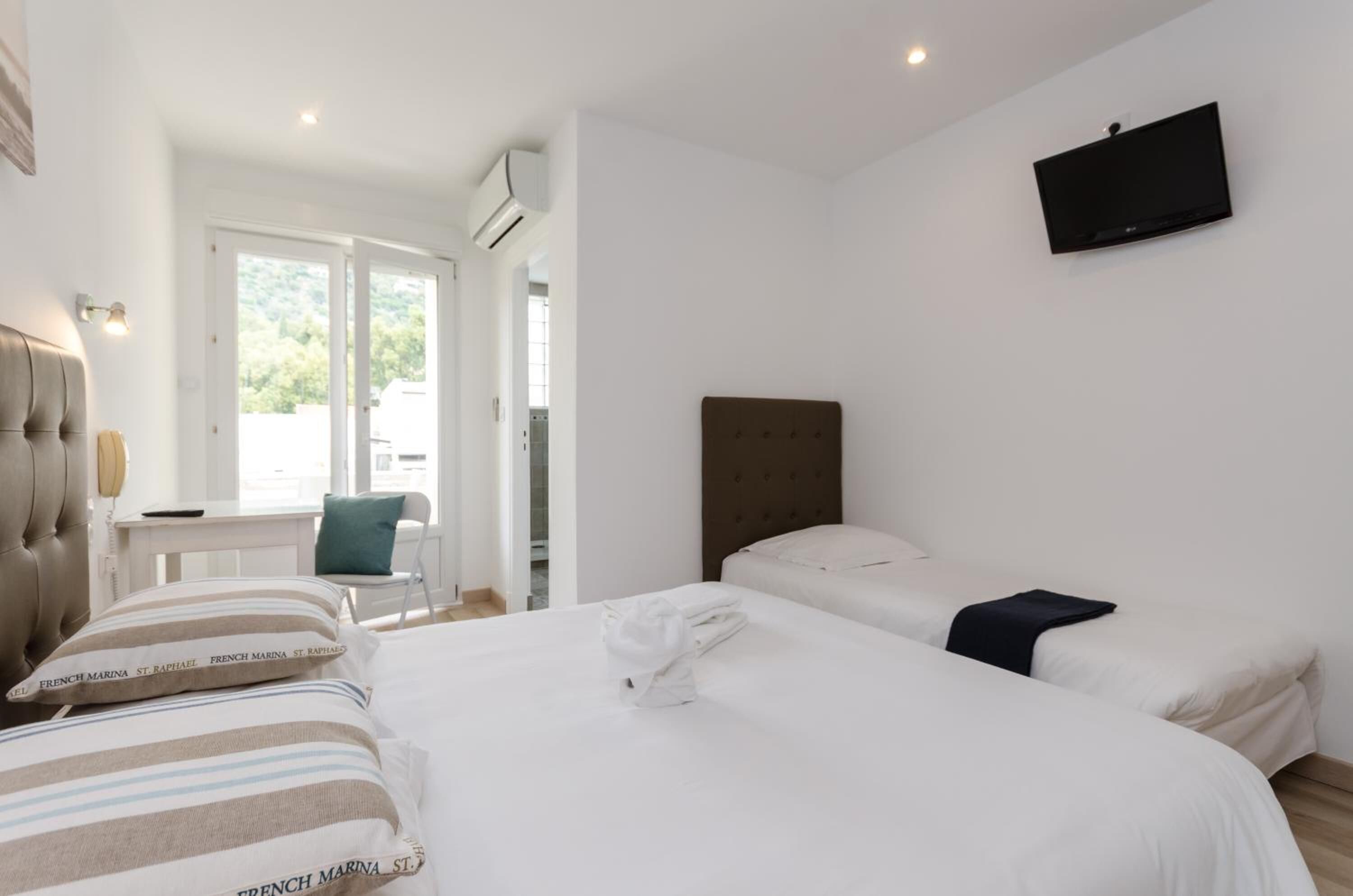 Habitación de hotel con dos camas, televisión y vistas al exterior.