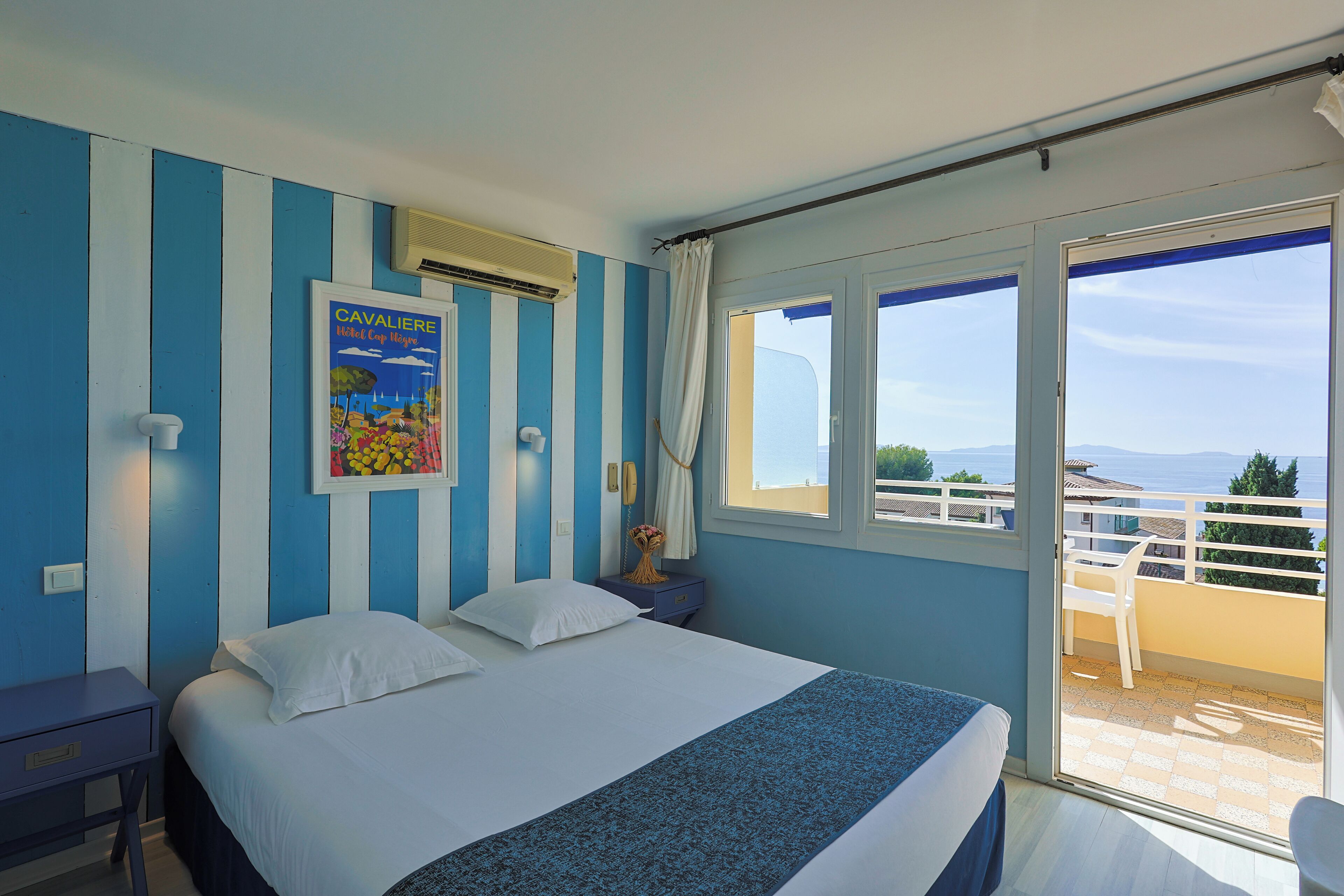 A hotel room with a bed, a nightstand, a poster, and a balcony with a view.