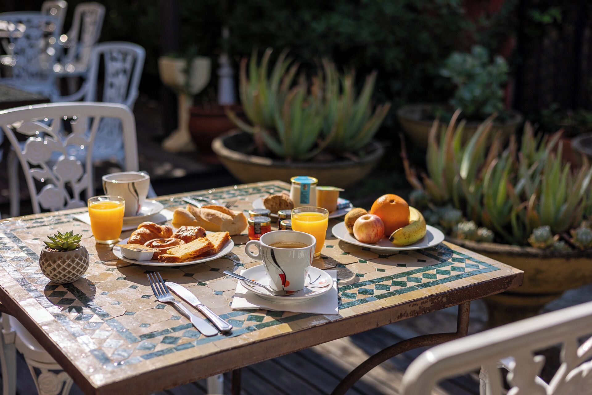 A table set with breakfast items including toast, fruit, and juice, surrounded by chairs and potted plants.