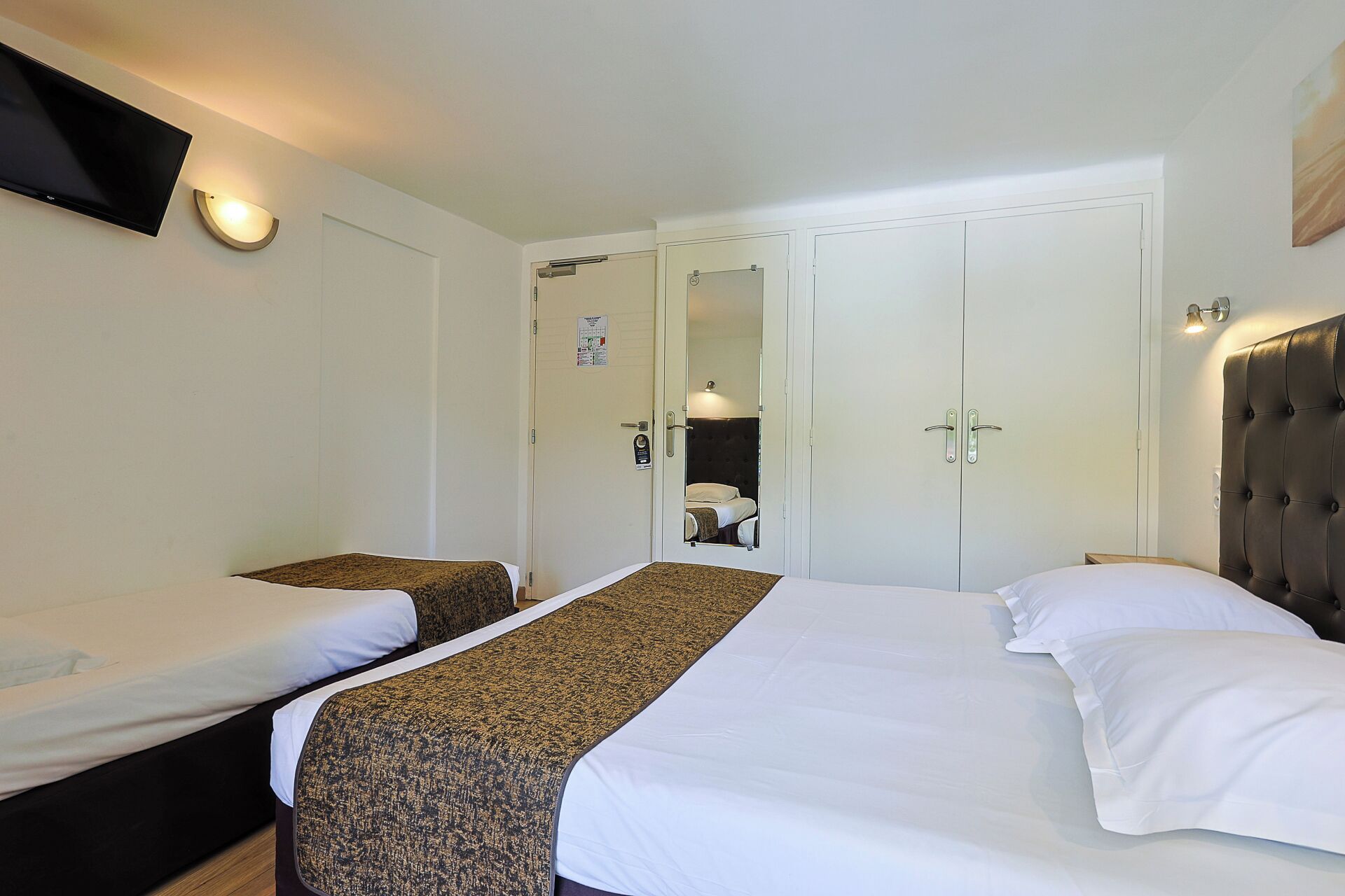 A hotel room with two beds, a flat-screen TV, a mirror, and a wardrobe.