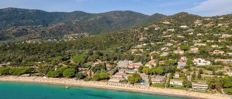 A coastal town with a beach, houses, and mountains in the background.