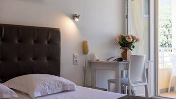 A hotel room with a tufted headboard, a desk with a telephone, a chair, and a vase with flowers.