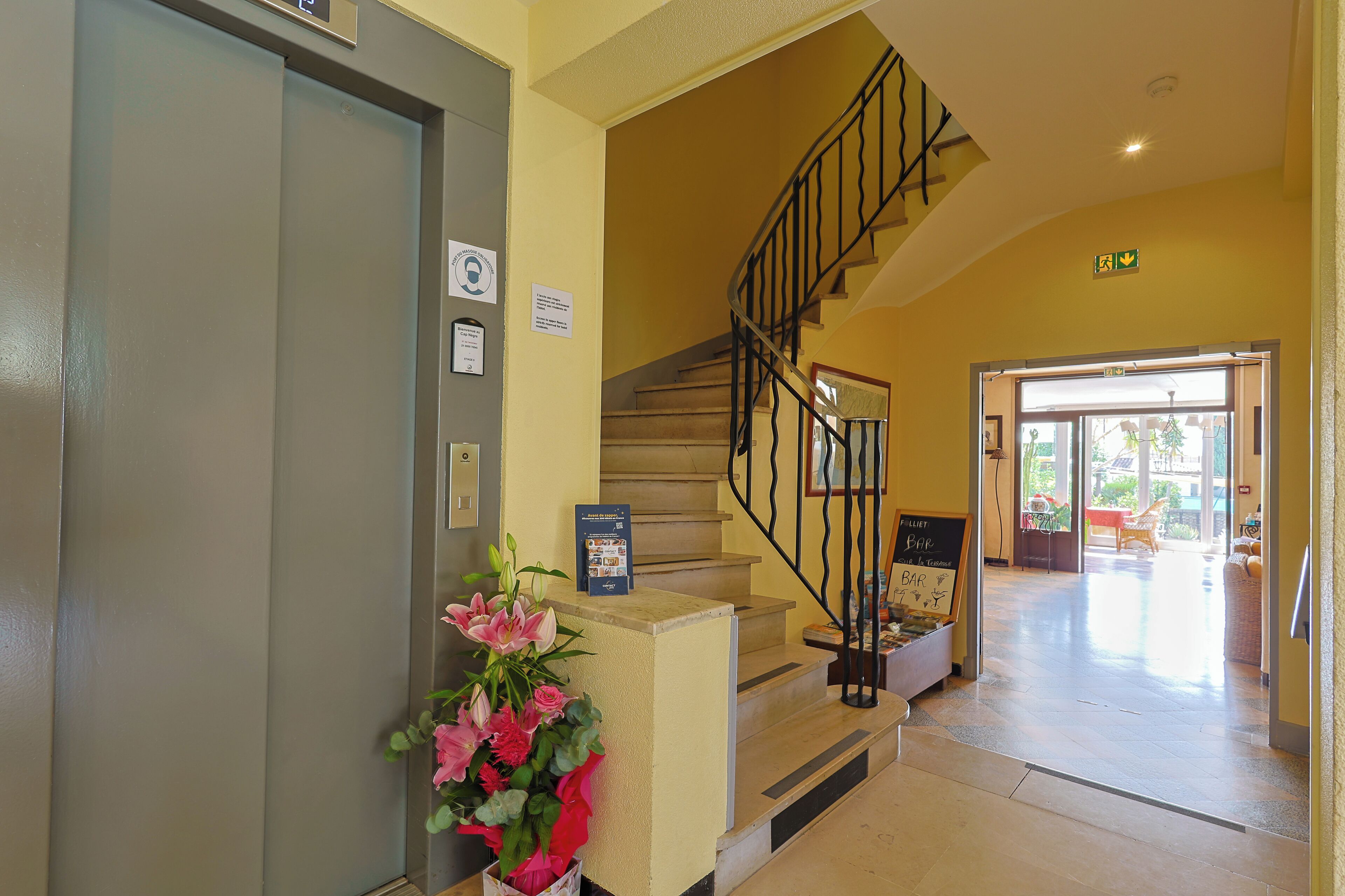 A hotel lobby with a staircase, a reception desk, and a flower arrangement.