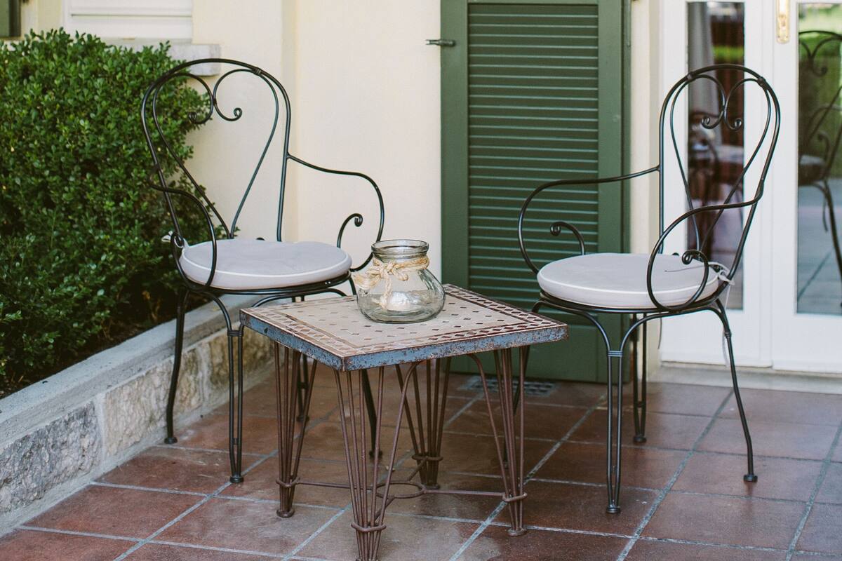 Eine Terrasse mit zwei Metallstühlen und einem kleinen Tisch, einer grünen Tür und einem Fenster mit Fensterläden.