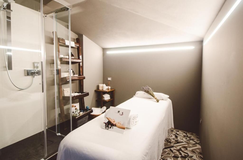 Un spa moderno con cabina de ducha de vidrio, una camilla de masaje y un pequeño estante de madera con artículos de aseo.