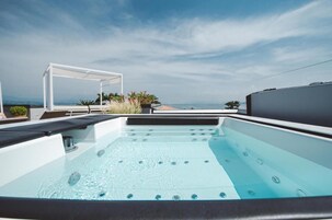 A rooftop hot tub with a clear view of the ocean and a white pergola structure.