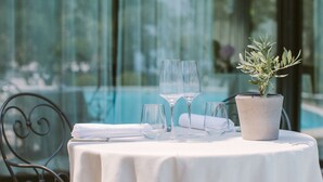Une table dressée avec des verres à vin et une plante en pot, avec une piscine en arrière-plan.