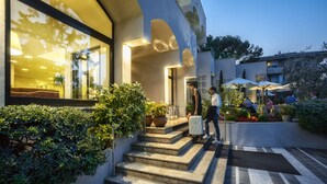Un bâtiment moderne avec un escalier menant à une entrée abritée, entouré de verdure et doté d’un espace extérieur aménagé pour s  ’asseoir.