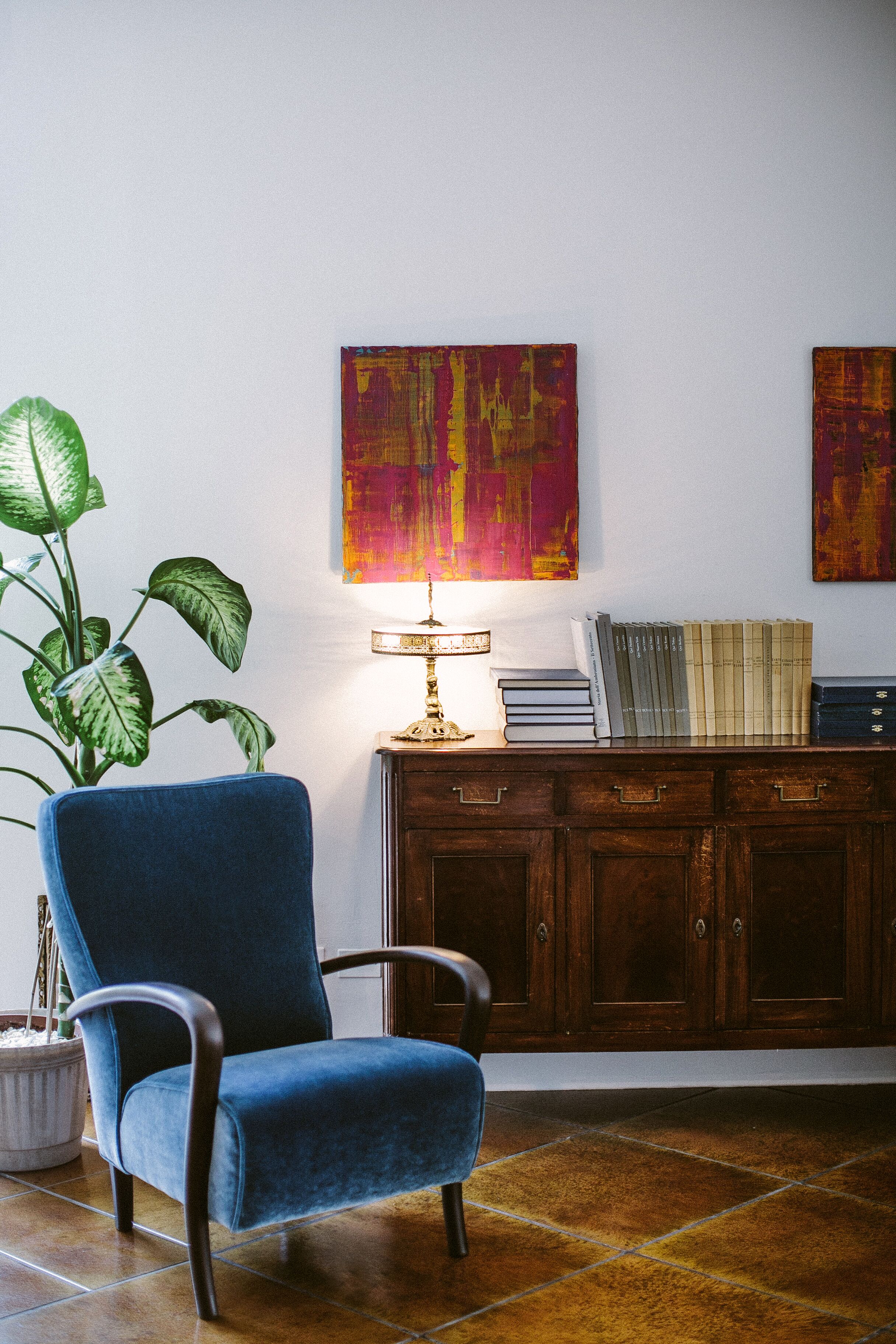 Ein Zimmer mit blauem Sessel, einer Holzkabine mit Büchern und einer Topfpflanze.