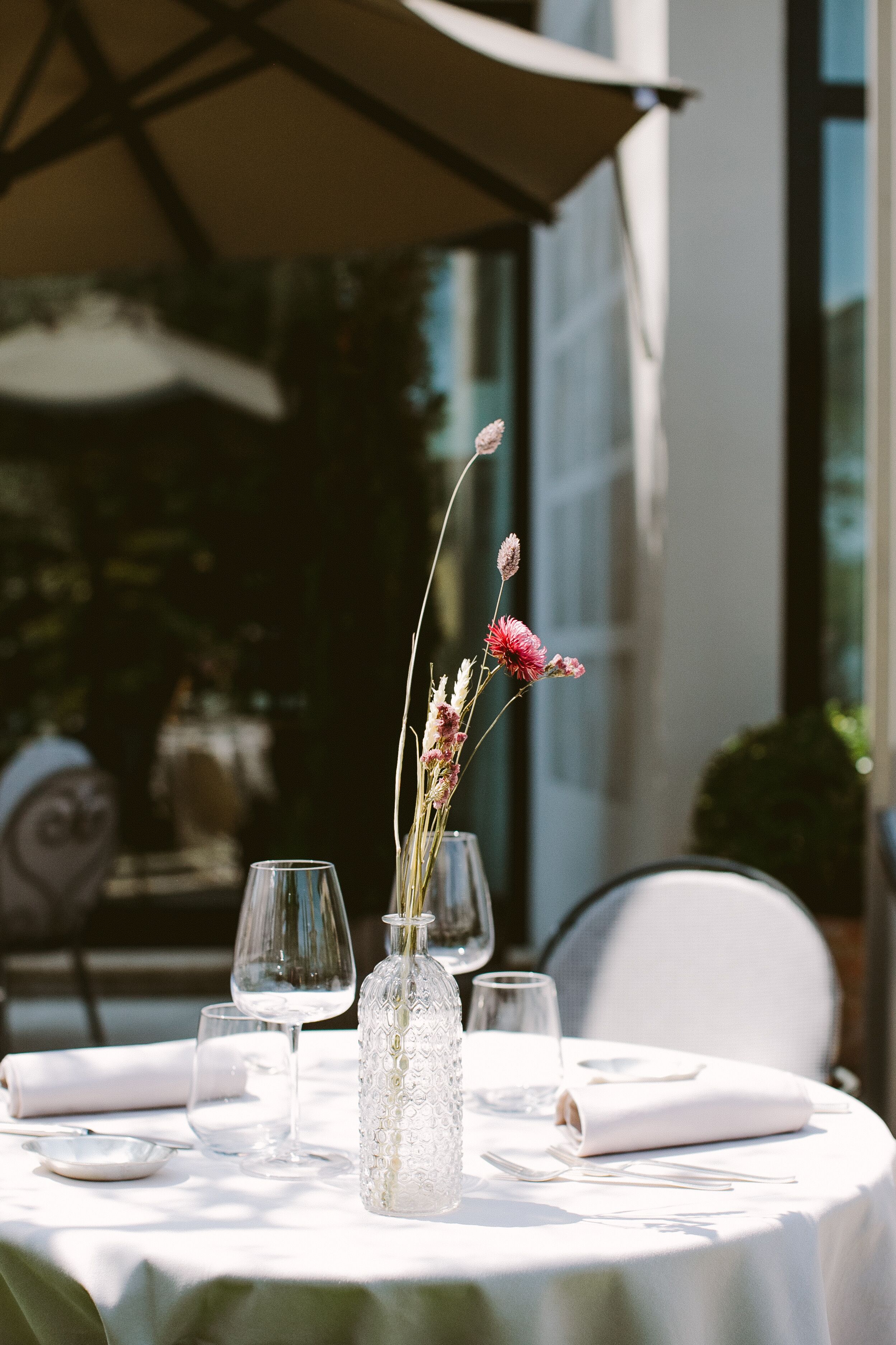 A table set for dining with a vase of flowers, clear glasses, and folded napkins.