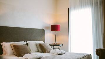 A neatly made bed with a grey headboard, a red lamp on a small table beside it, and a view of a window with sheer curtains.