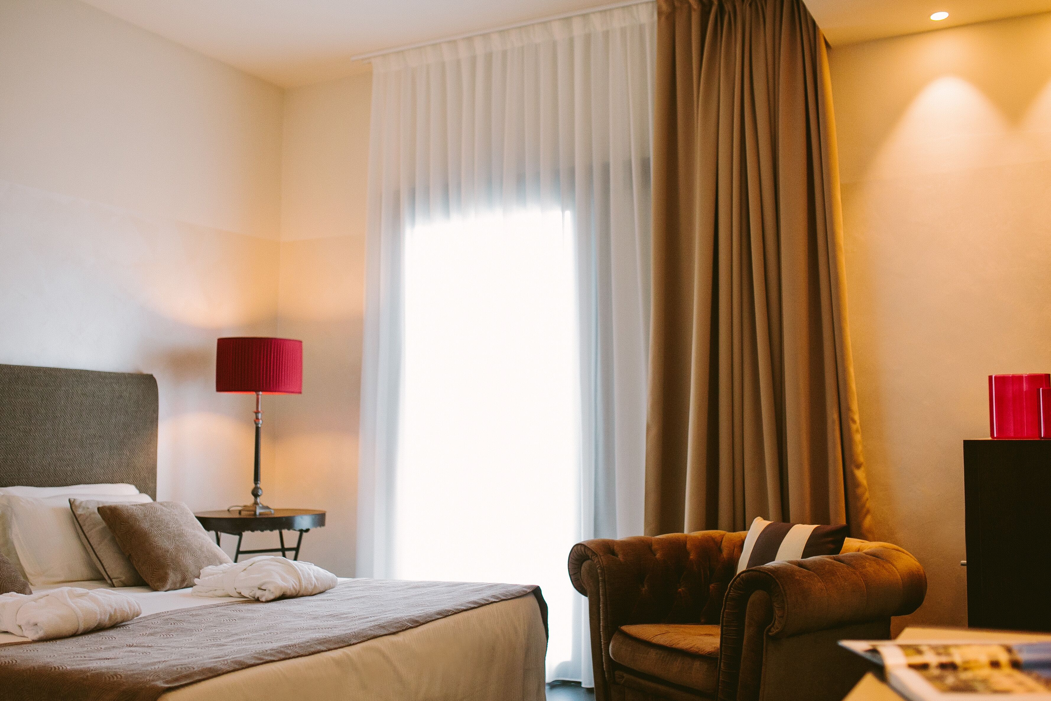 A hotel room with a bed, a chair, a nightstand, and a lamp.