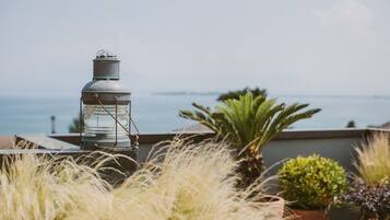 A rooftop terrace with a metal lantern, potted plants, and a view of the sea.