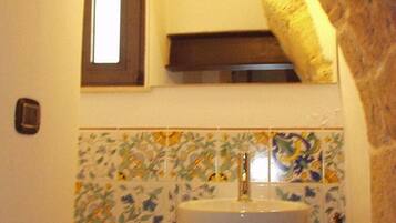 Un bagno con un lavandino bianco, uno specchio sopra e uno schienale piastrellato.