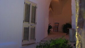 Um corredor arqueado com uma porta, uma janela, um banco e um vaso de plantas.