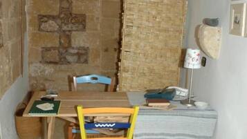 A small, rustic room with a stone wall, a wooden table, a chair, and a bed with a striped blanket.