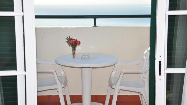 A balcony with a white table and chairs, a vase with flowers, and a view of the sea. - Vila Marta (Funchal)