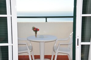 A balcony with a white table and chairs, a vase with flowers, and a view of the sea. - Vila Marta (Funchal)