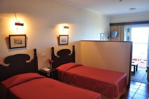A hotel room with two single beds, a bedside table with a telephone, and a small table with a vase of flowers.