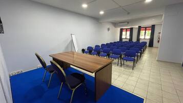 A conference room with a wooden table, blue carpet, and rows of blue chairs.