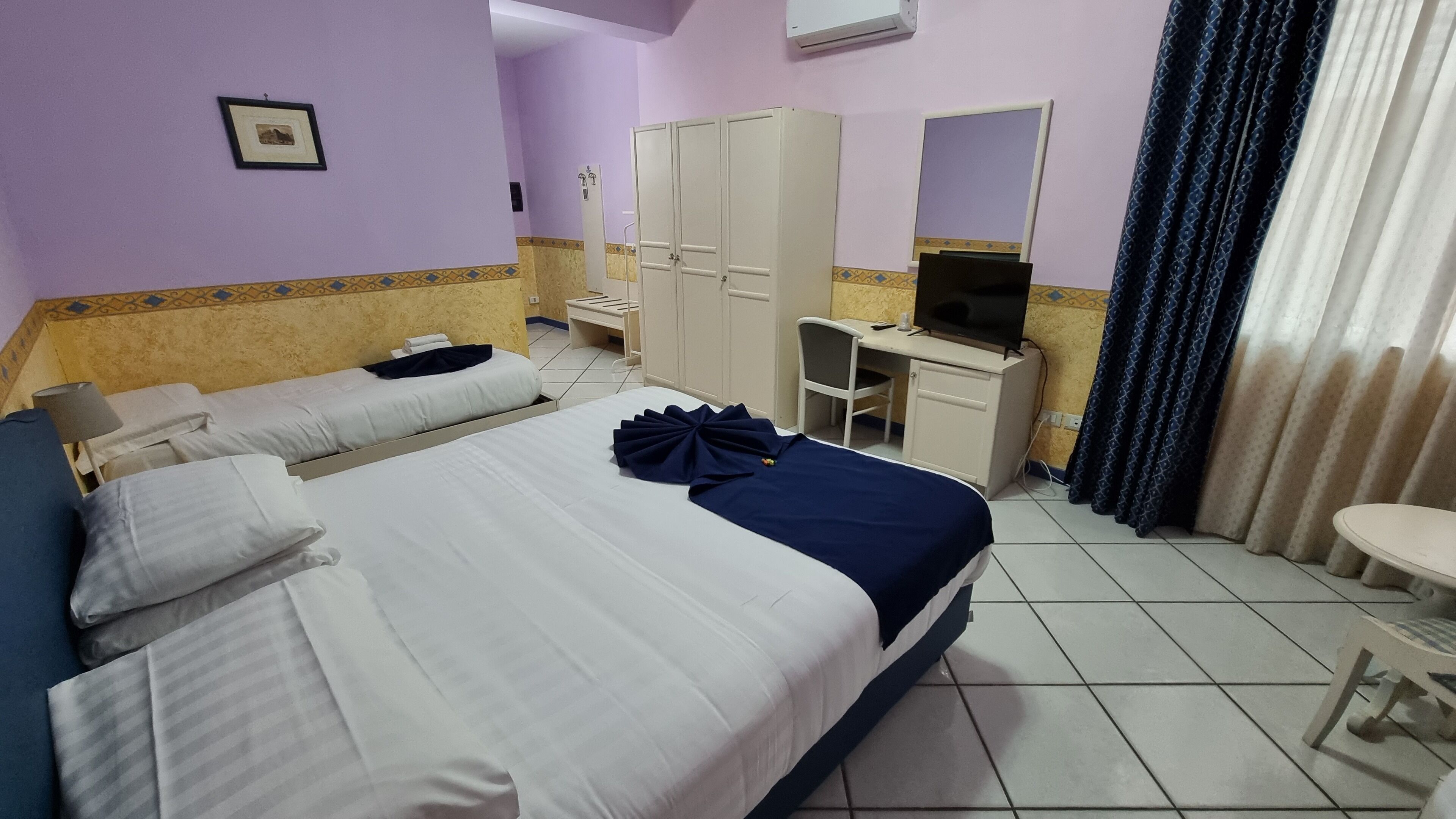 Una habitación de hotel con dos camas, un escritorio, una silla, un televisor y un armario.