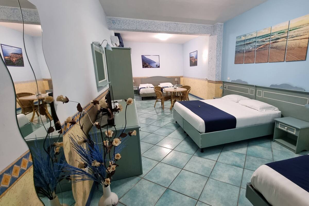 Una habitación de hotel con cama, mesita de noche, espejo y un florero con flores.