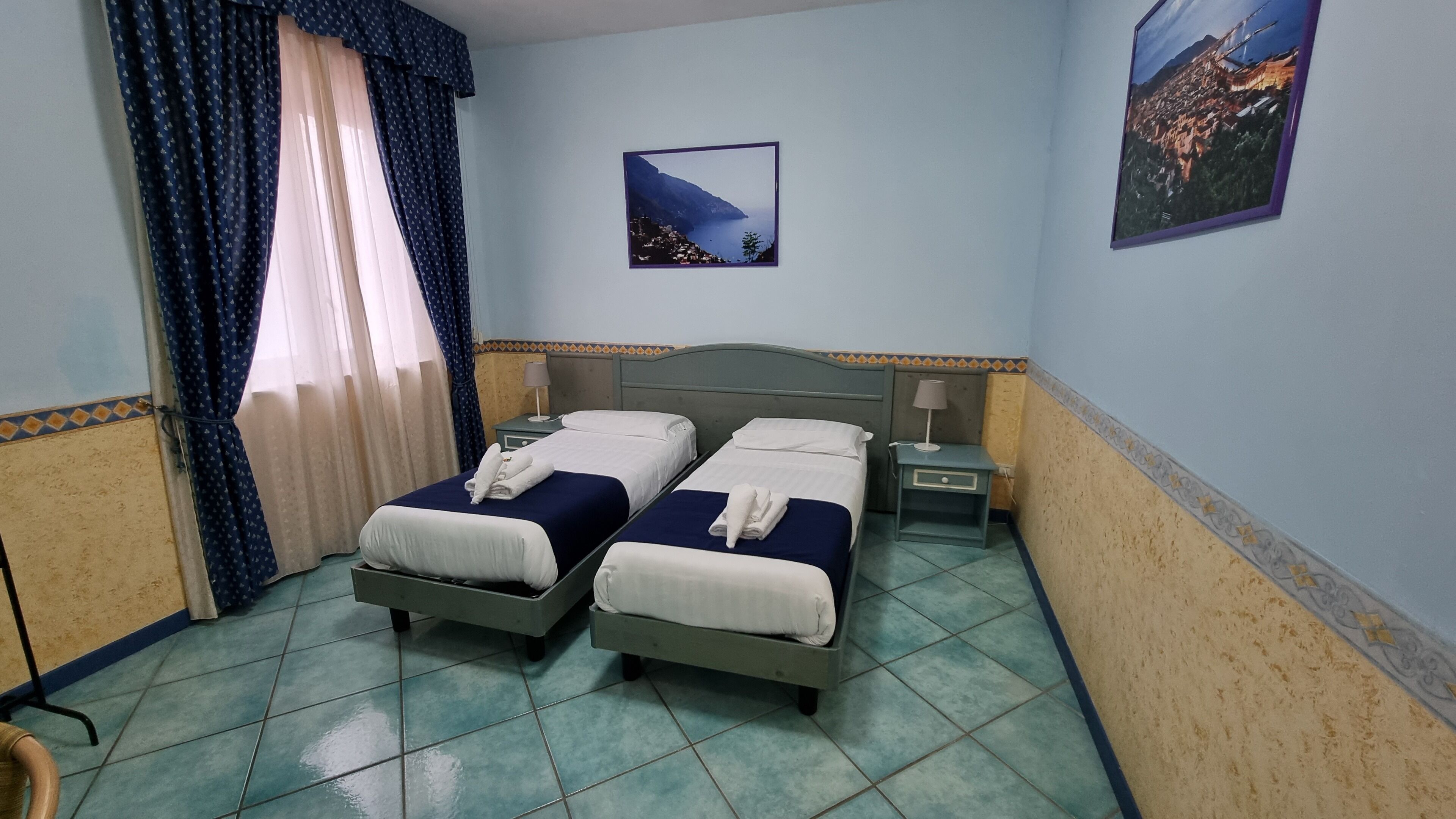 Habitación de hotel con dos camas, una mesita de noche, una lámpara y un cuadro en la pared.
