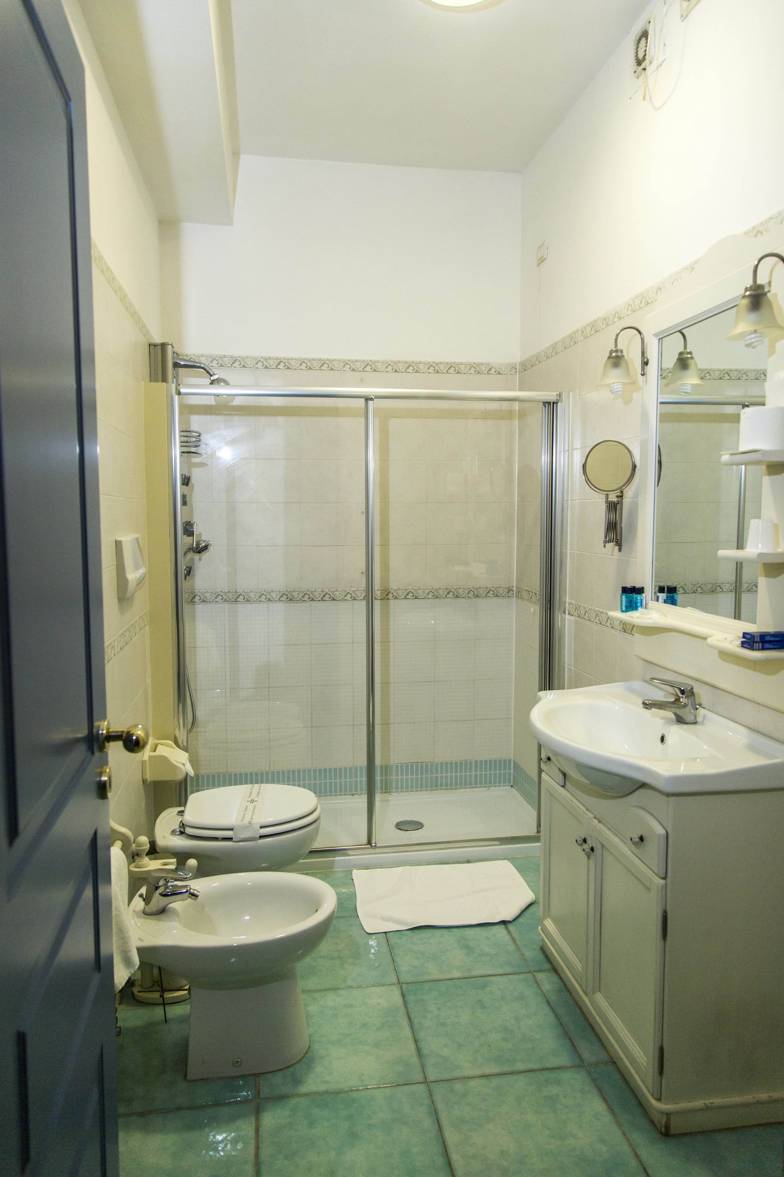 A bathroom with a shower, two toilets, a sink, and a mirror.
