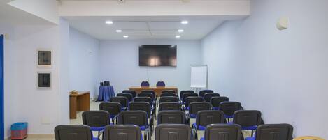 A conference room with rows of chairs, a table, a projector screen, and a whiteboard.