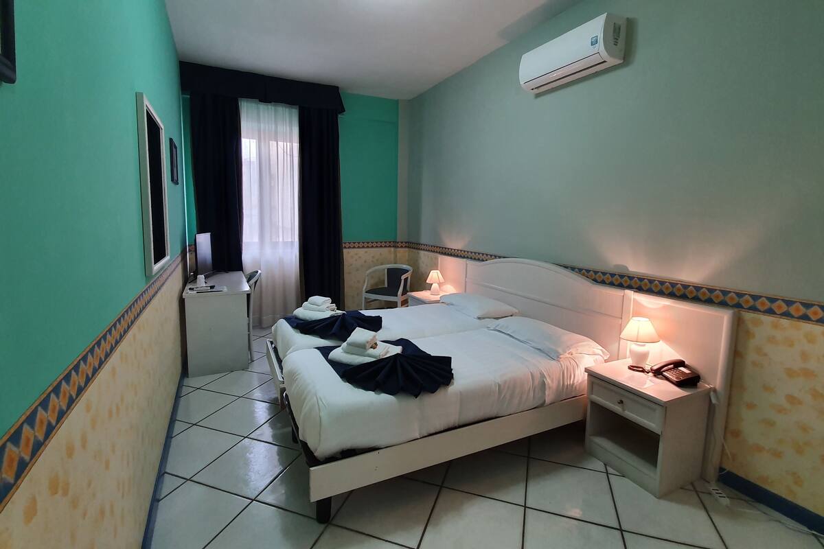 Una habitación de hotel con cama, mesita de noche, lámpara y aire acondicionado.
