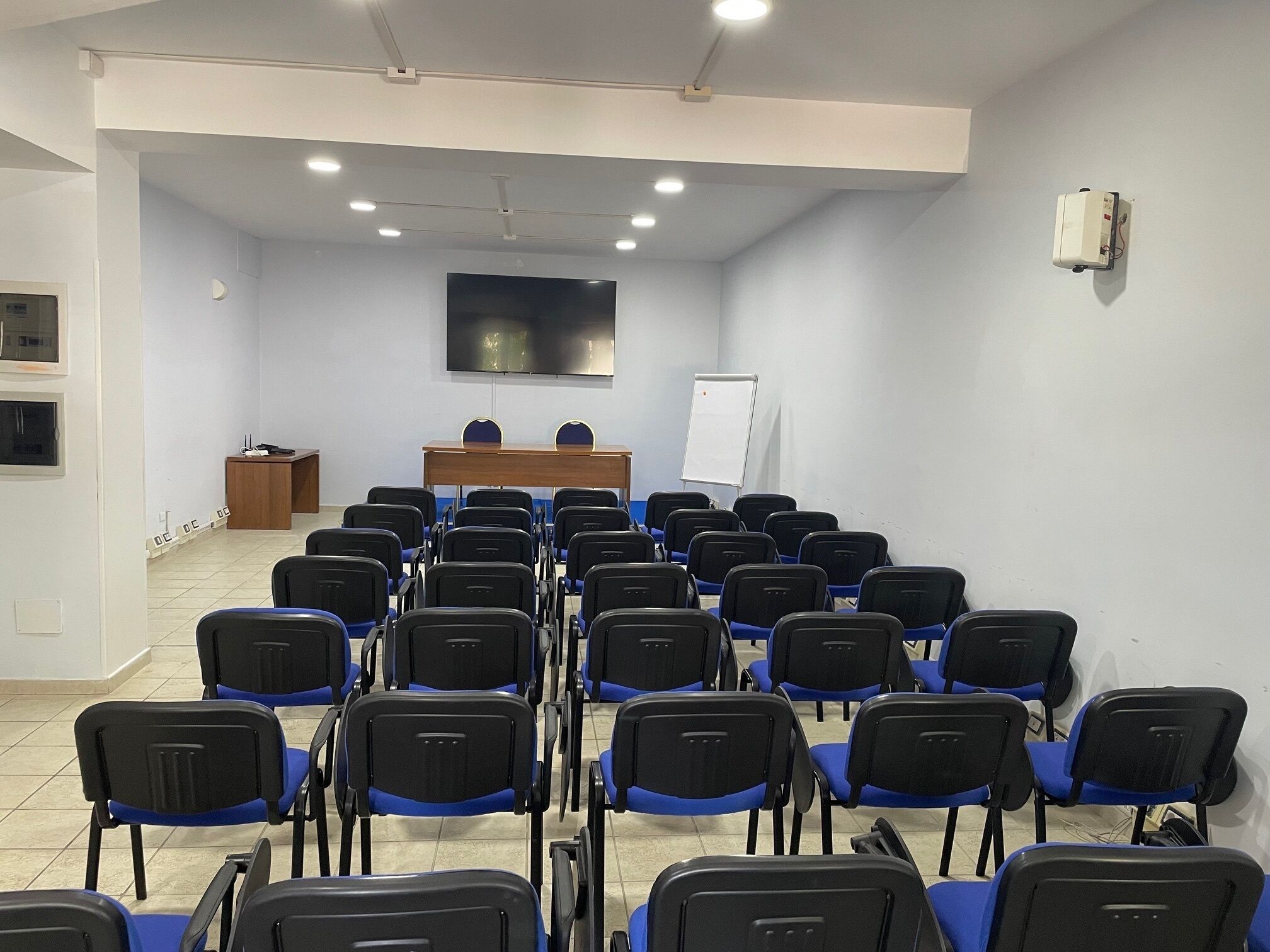 A conference room with rows of chairs, a whiteboard, and a flat-screen TV on the wall.