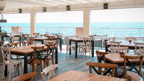 Ein Restaurant mit Holztischen und -stühlen, großen Fenstern und Blick auf das Meer.