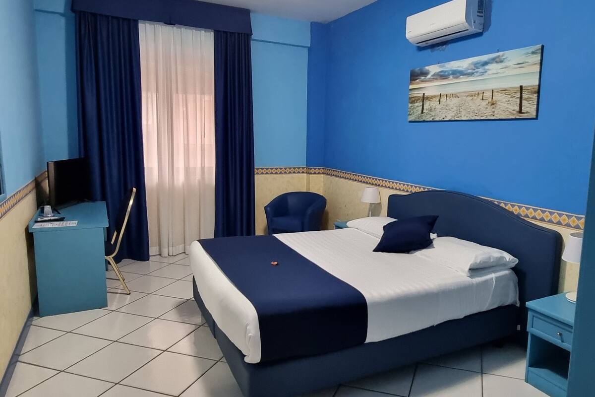 Una habitación de hotel con cama, escritorio, silla, televisor y un cuadro en la pared.
