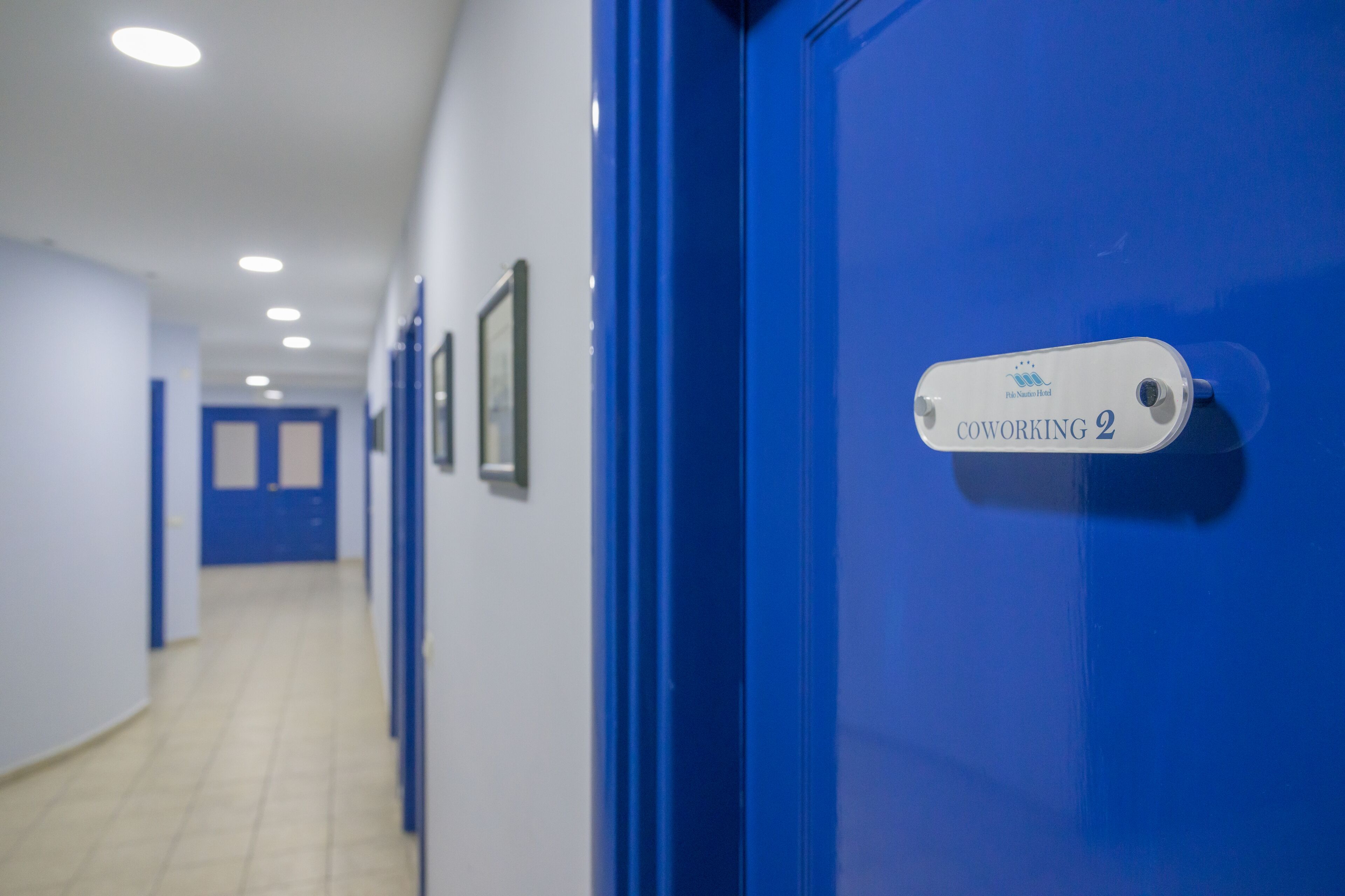 A hallway with blue doors, a sign reading "Coworking 2", and framed pictures on the walls.