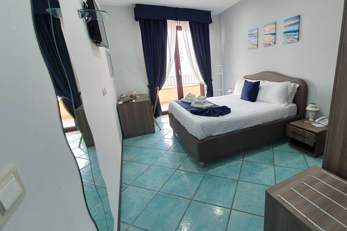 Una habitación de hotel con cama, mesita de noche, cortinas en la ventana y vistas al exterior.