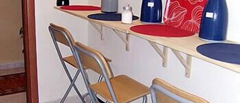 Una pequeña kitchenette con una encimera, un hervidor, una cafetera y dos sillas.