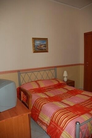 Un dormitorio con cama, mesita de noche, lámpara y un cuadro en la pared.