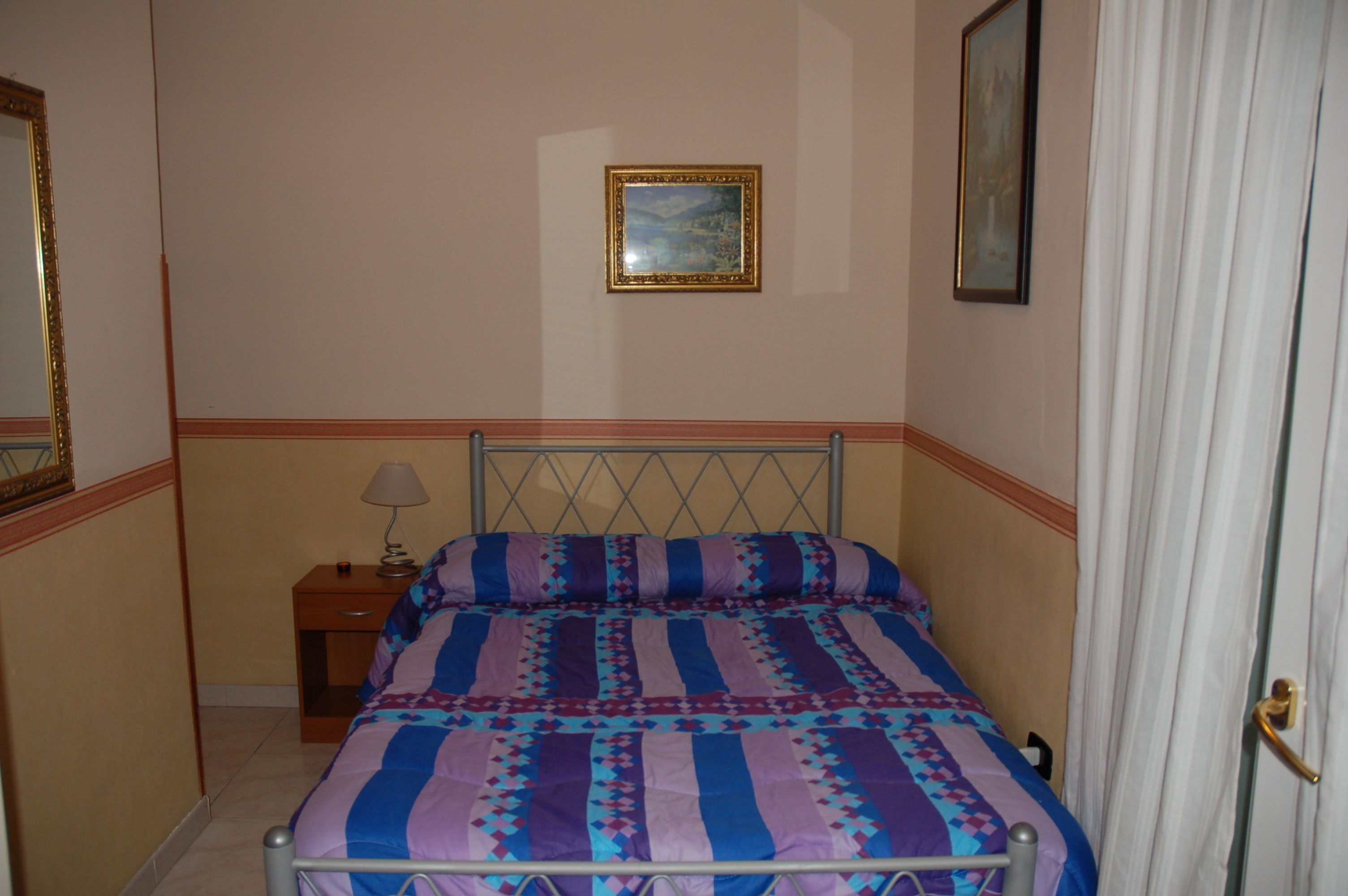 A bedroom with a bed, a nightstand, a lamp, and a painting on the wall.