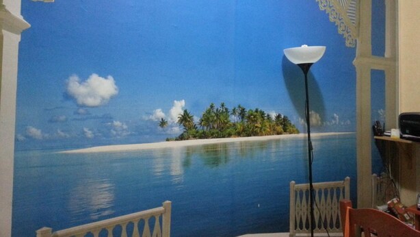 Une pièce décorée d’une fresque représentant une scène de plage, avec une lampe blanche et deux chaises.